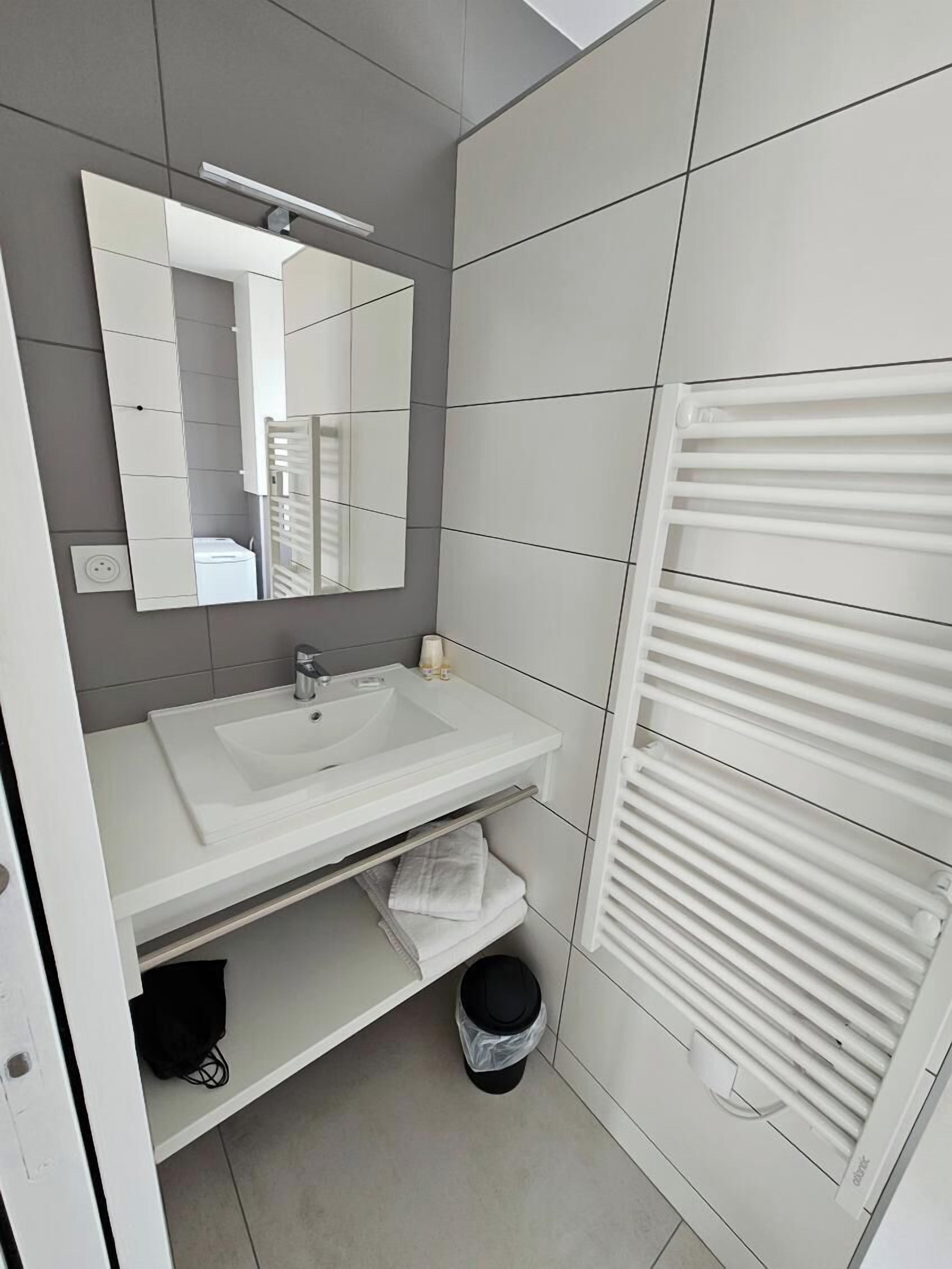 A modern bathroom with a white sink, mirror, and towel rack.