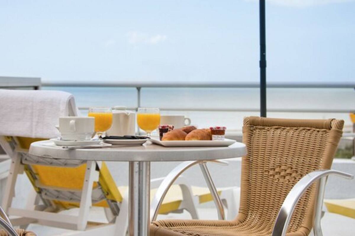 Une table avec des aliments pour le petit-déjeuner, une chaise en osier et une vue sur la mer.