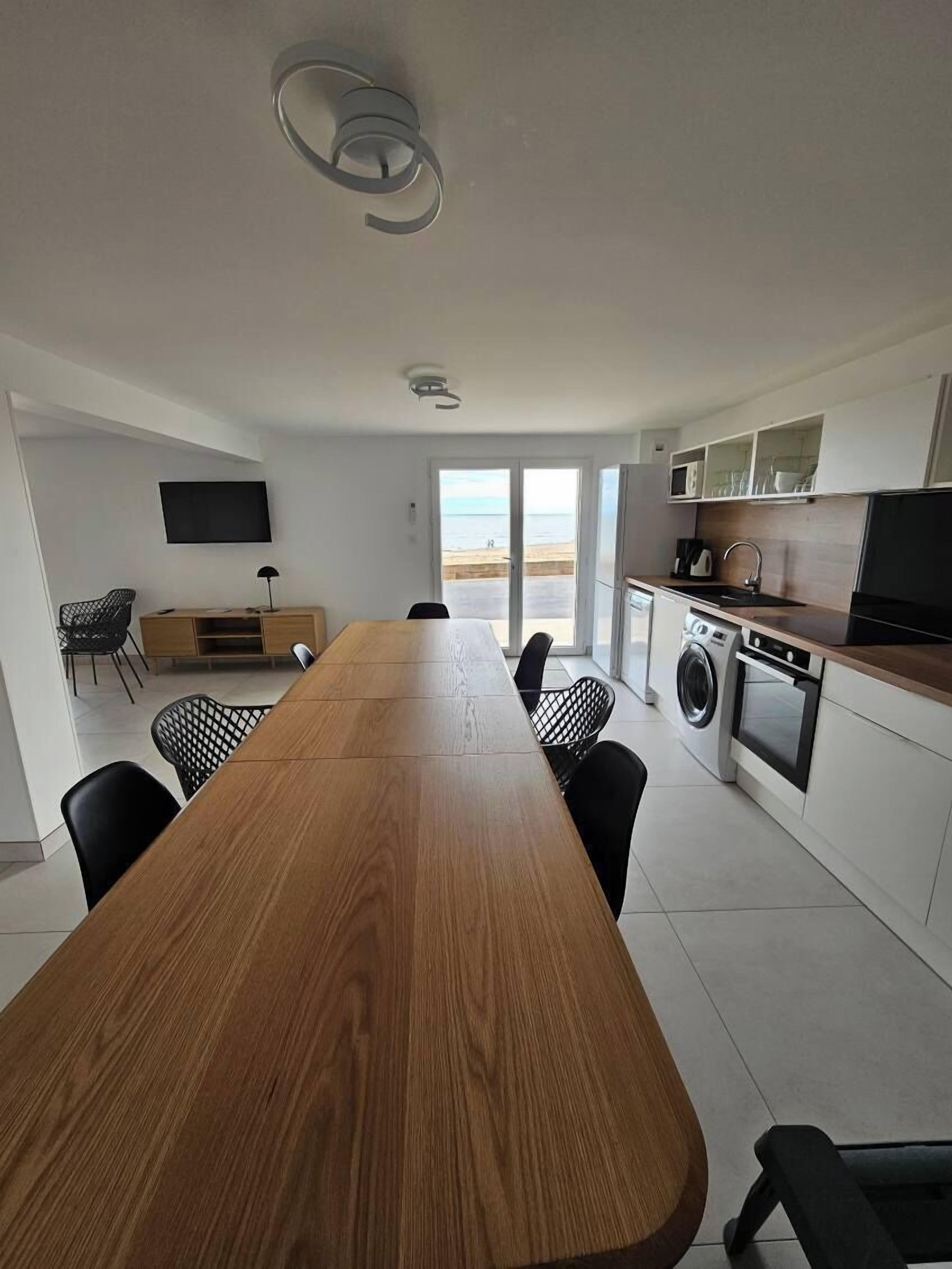 A modern kitchen with a wooden dining table, black chairs, a built-in oven, and a washing machine.