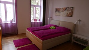 Une chambre à coucher avec un lit, une table de chevet, une lampe, une fenêtre avec des rideaux et un tableau au mur.