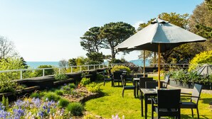 An outdoor patio with tables and chairs, surrounded by a garden with various plants and flowers. - The Cliffden Hotel (Teignmouth)