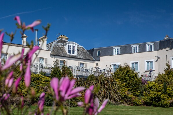 A large, multi-story building with a prominent central tower, surrounded by lush greenery and flowering plants. - The Cliffden Hotel (Teignmouth)