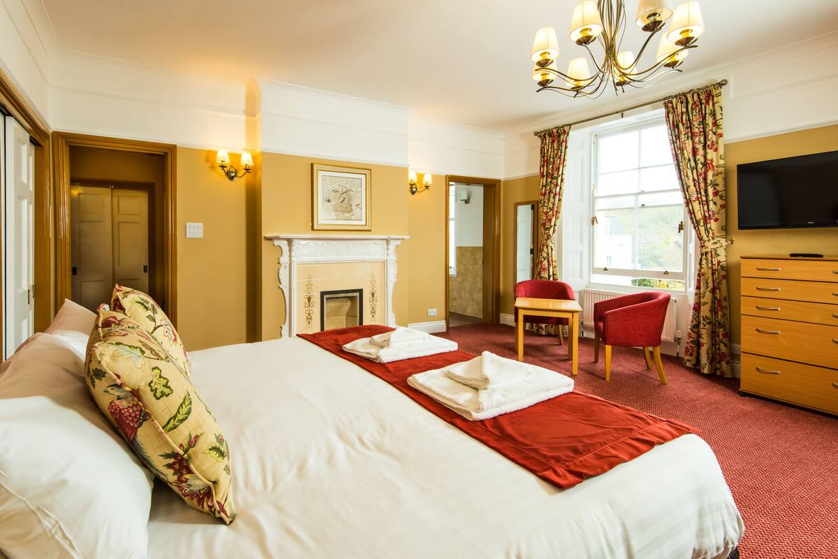 A hotel room with a large bed, a fireplace, a television, and a desk with a chair.
