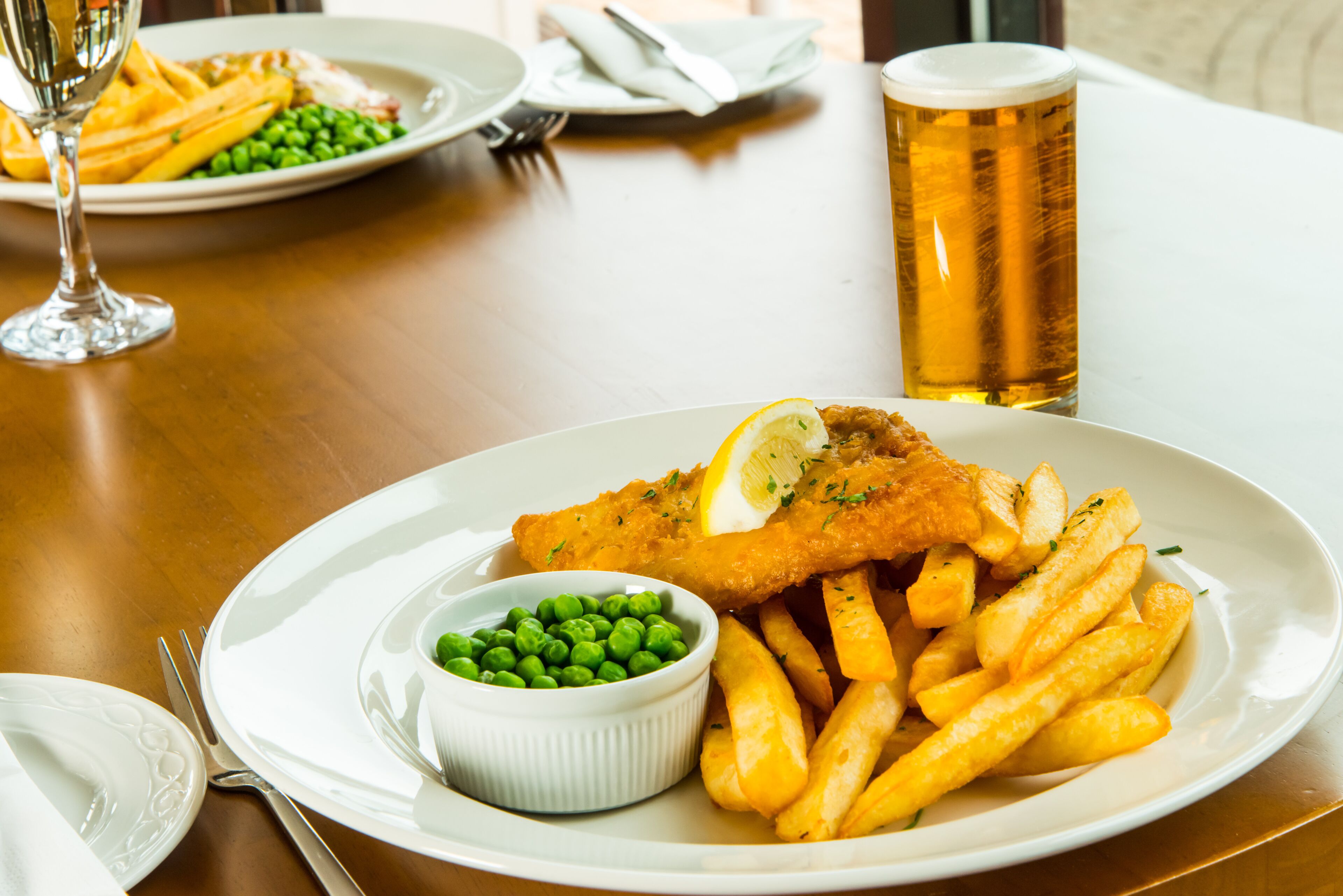 A plate of fish and chips with peas and a glass of beer on a wooden table.