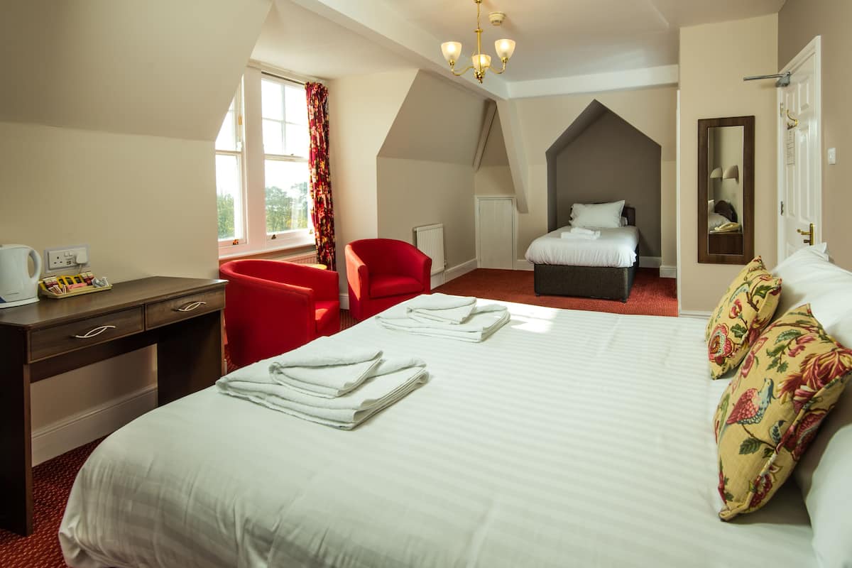 A hotel room with a large bed, a desk with a telephone, a red chair, and a window with curtains.