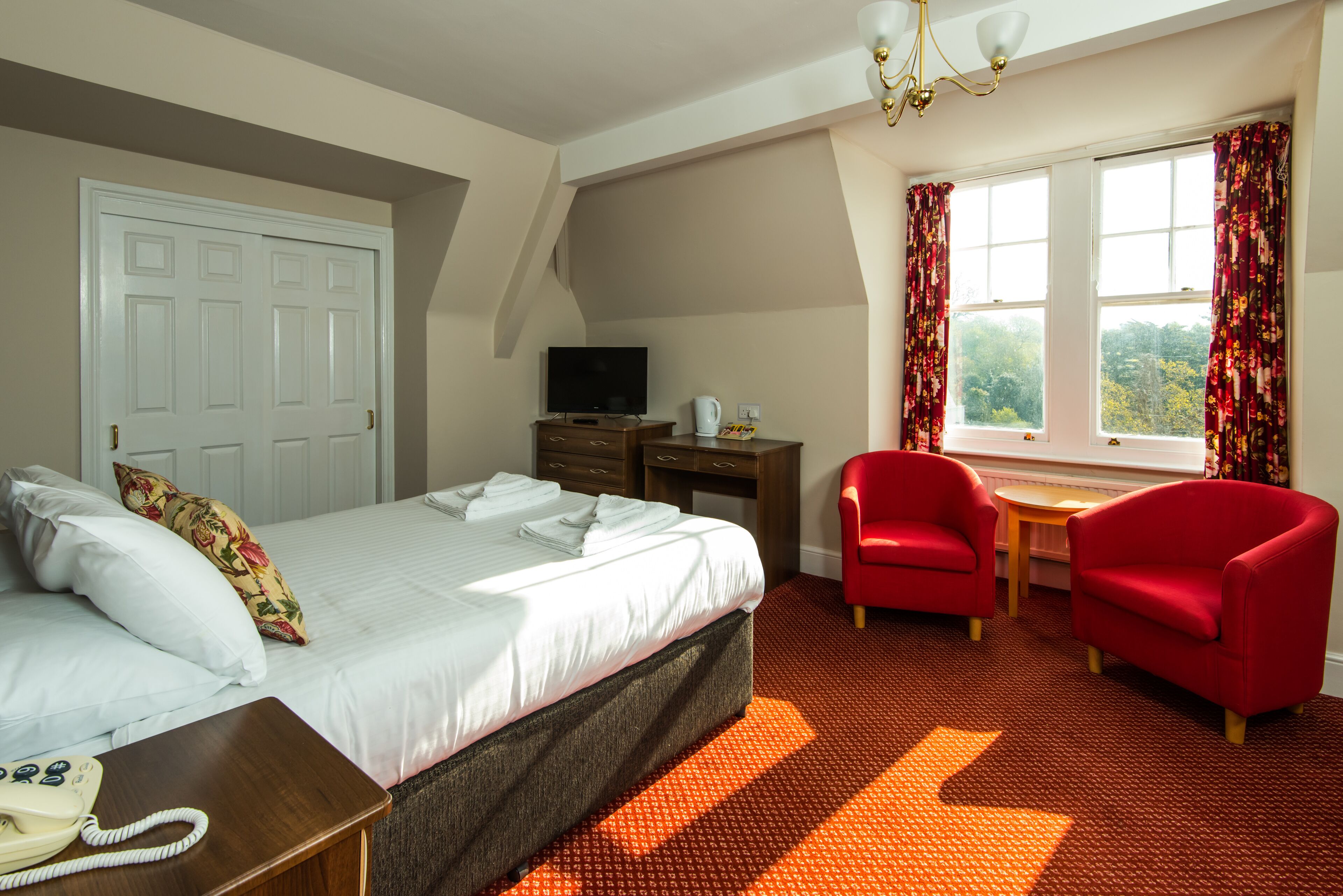 Een hotelkamer met een bed, een bureau, een televisie, een telefoon en twee rode stoelen.
