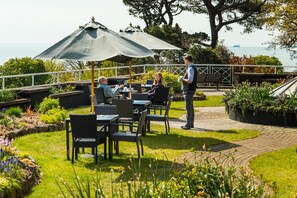 An outdoor seating area with tables and chairs, a waiter, and a view of the sea. - The Cliffden Hotel (Teignmouth)