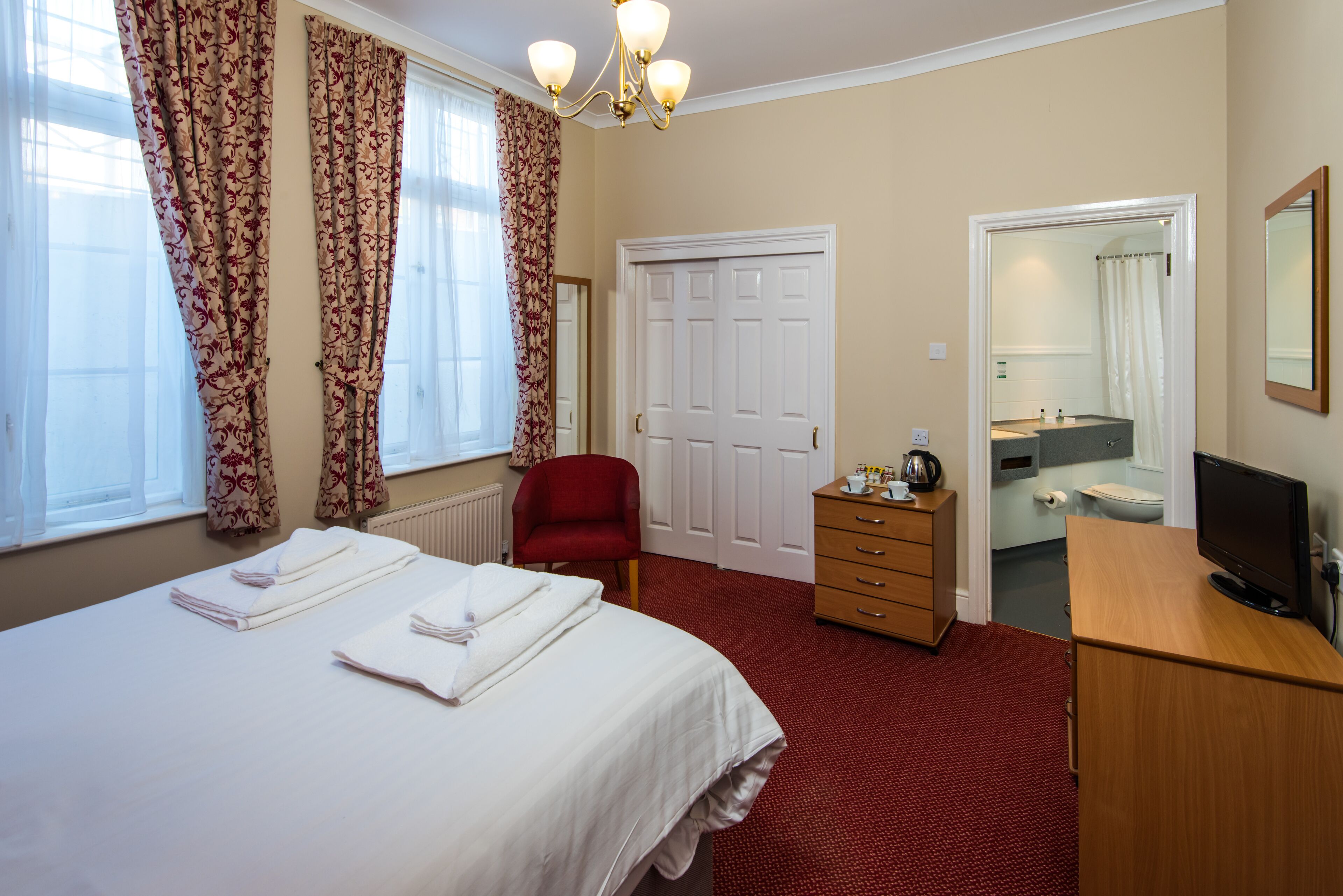Een hotelkamer met een bed, een rode stoel, een houten dressoir, een televisie en een badkamer die door een open deur zichtbaar is.