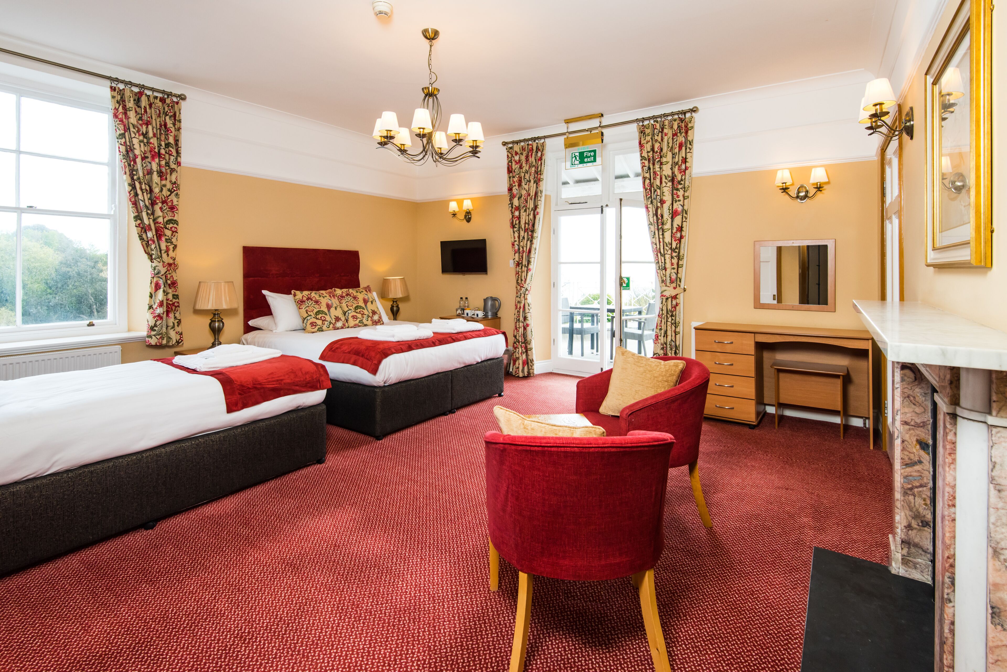 A hotel room with two beds, a desk, a chair, a TV, and a view of the outdoors.