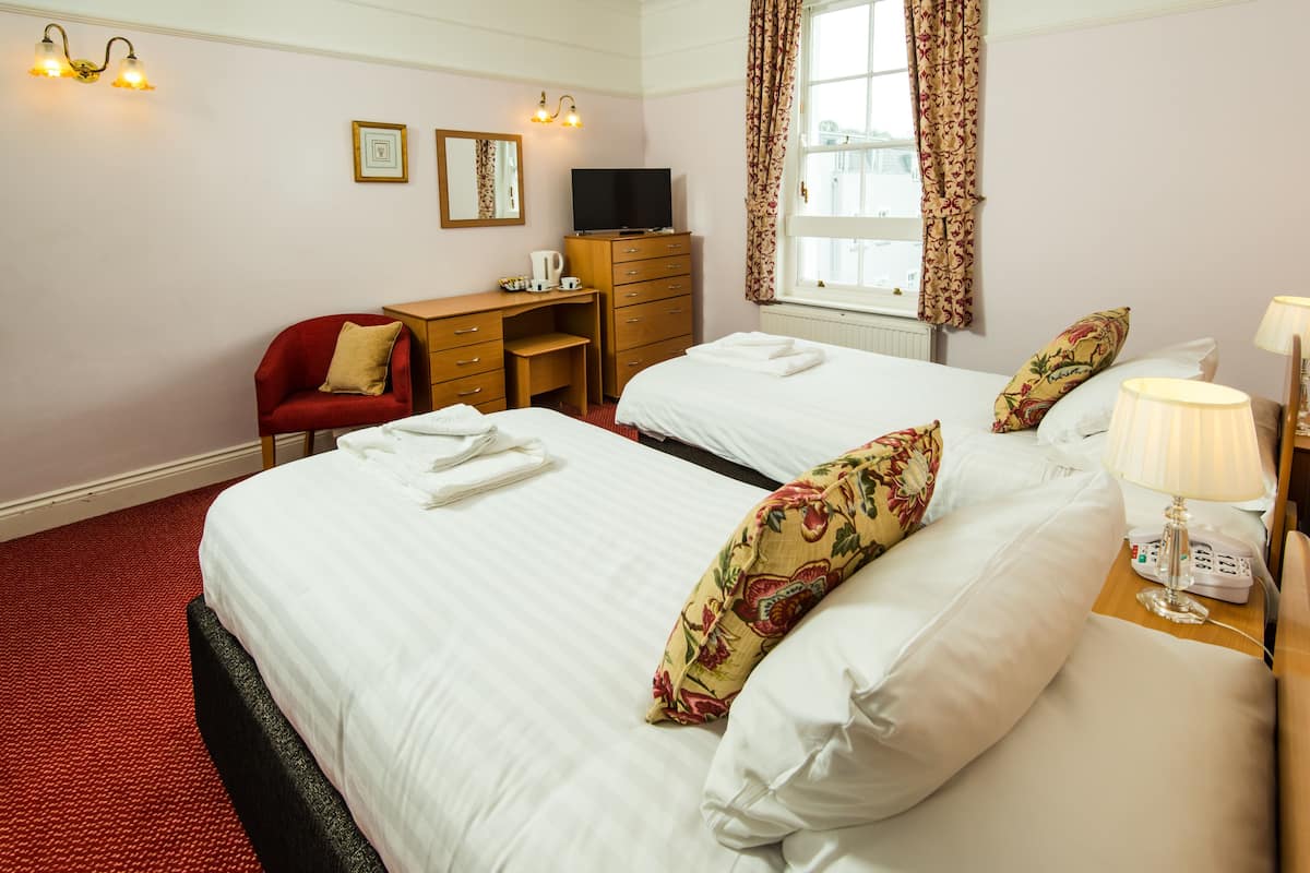 A hotel room with two beds, a desk, a chair, a TV, and a window with curtains.