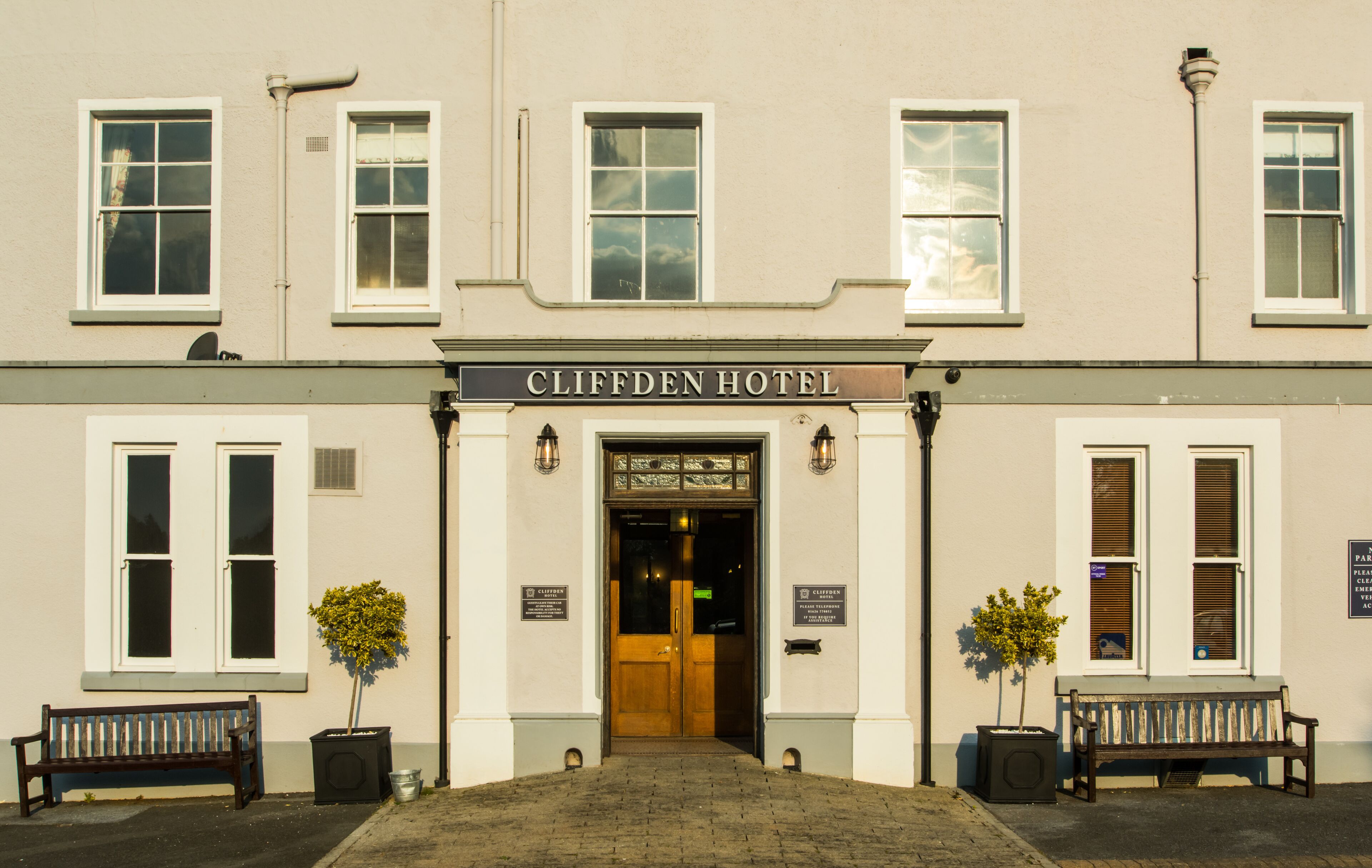 The front of Cliffden Hotel with a double door entrance, two potted plants, and a bench on either side.