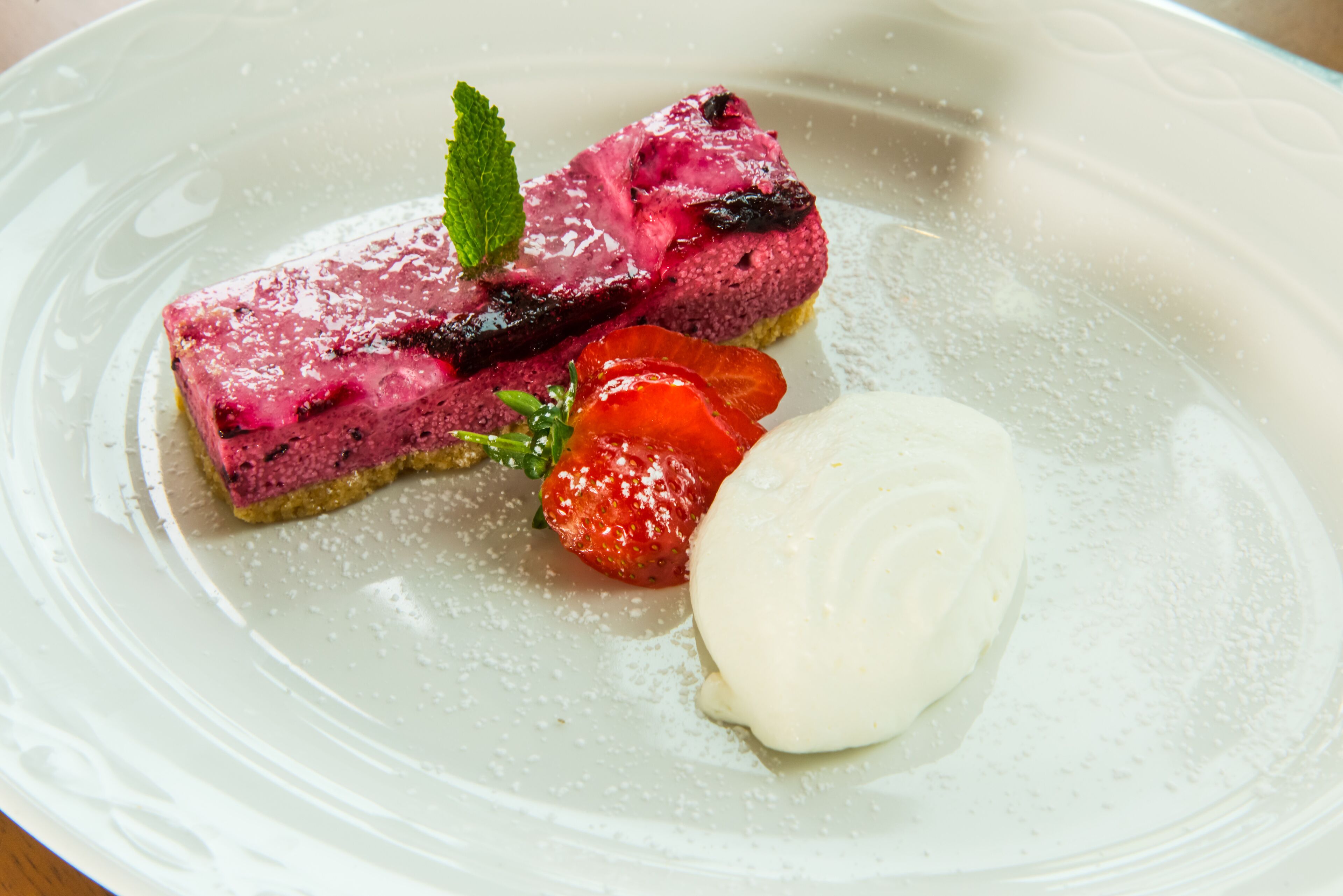 Un piattino con una fetta di crostata di frutti di bosco, una fragola e una pallina di gelato.