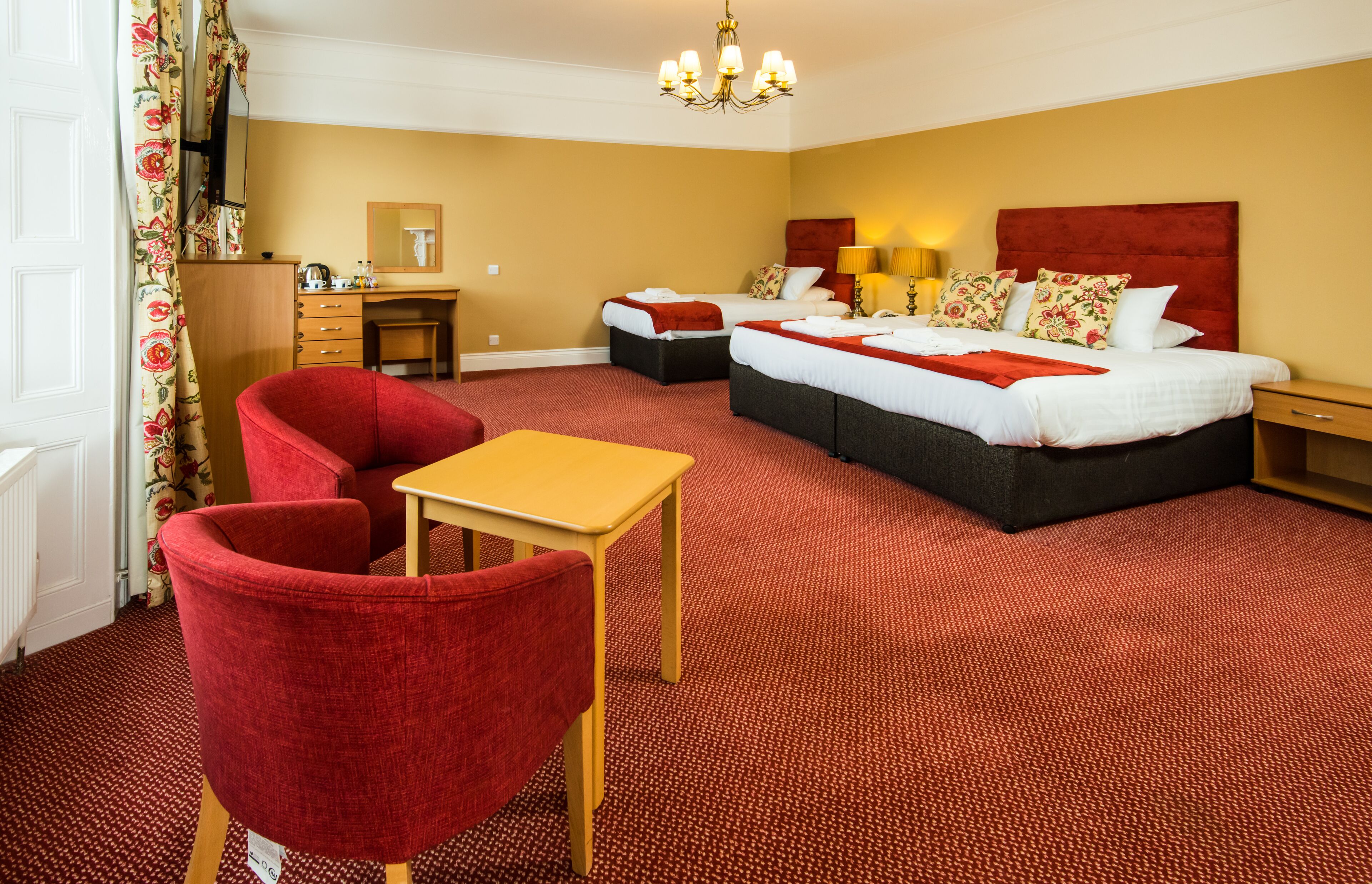 A hotel room with a large bed, two bedside tables, a desk, a chair, and a red armchair.