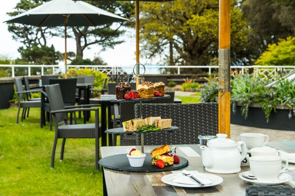 An outdoor dining area with a tiered dessert stand, tables with chairs, and a view of the outdoors.