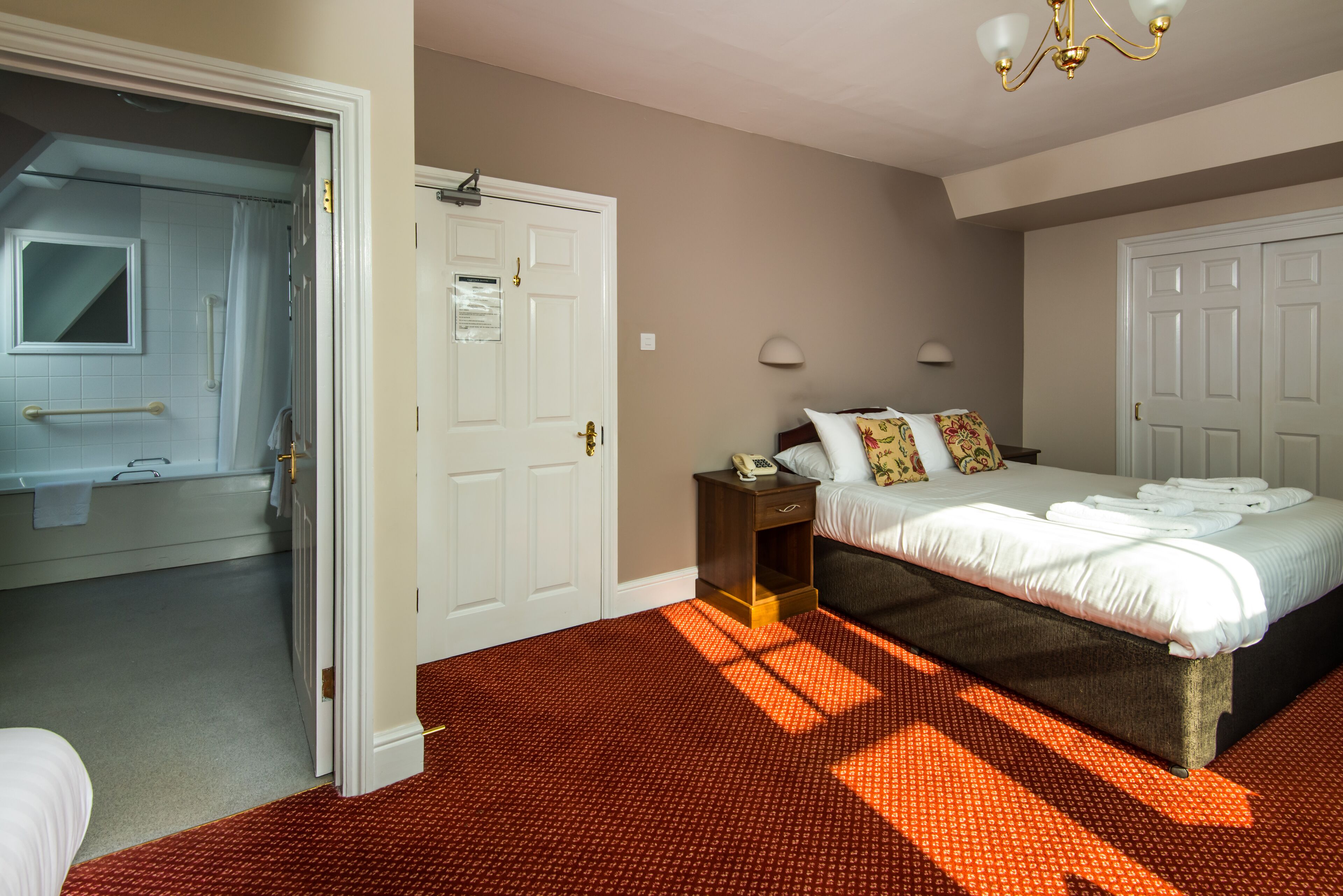 A hotel room with a bed, bedside table, and a bathroom visible through an open door.