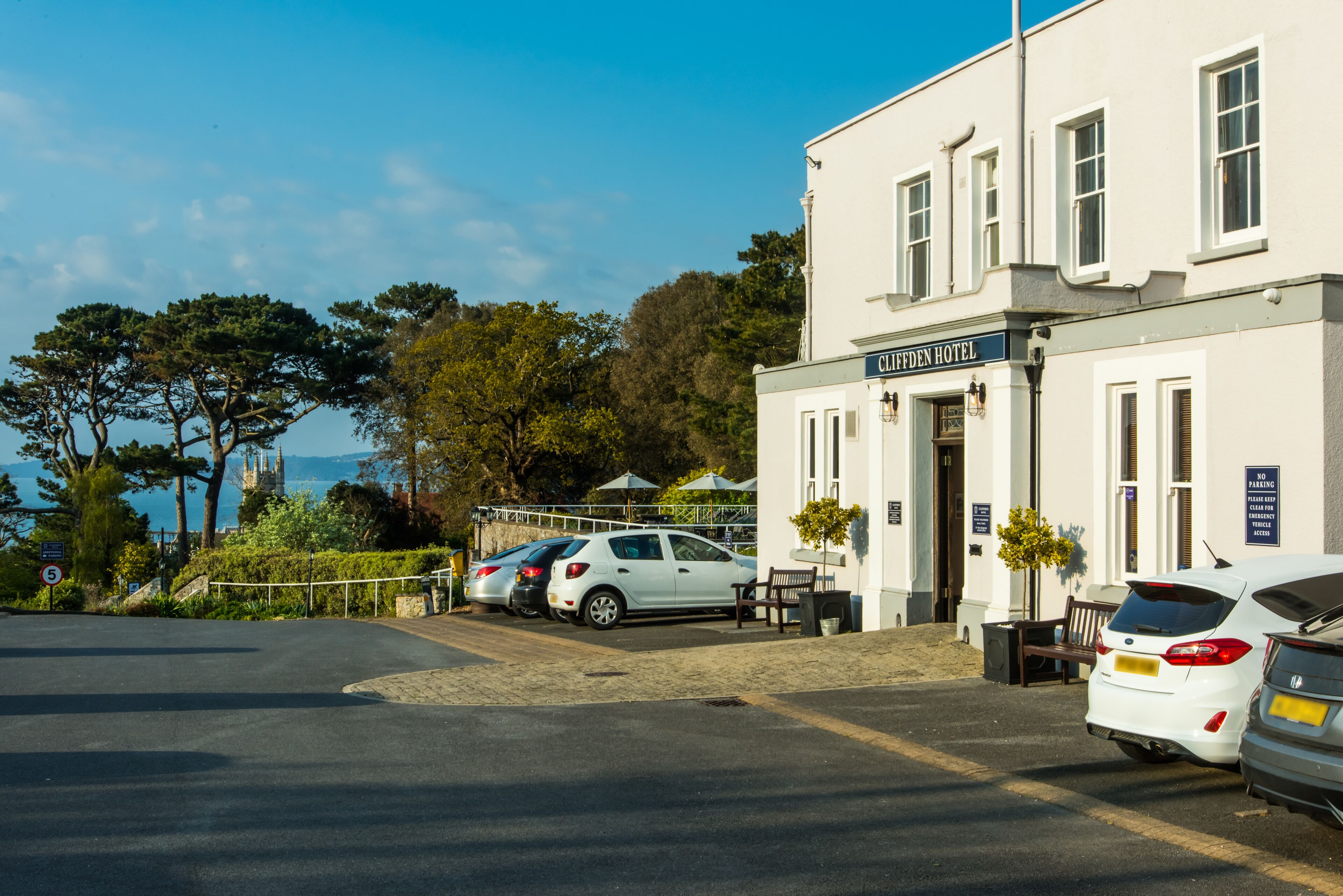 A hotel named "Clifff Hotel" with a parking area, a bench, and a view of trees and a body of water.
