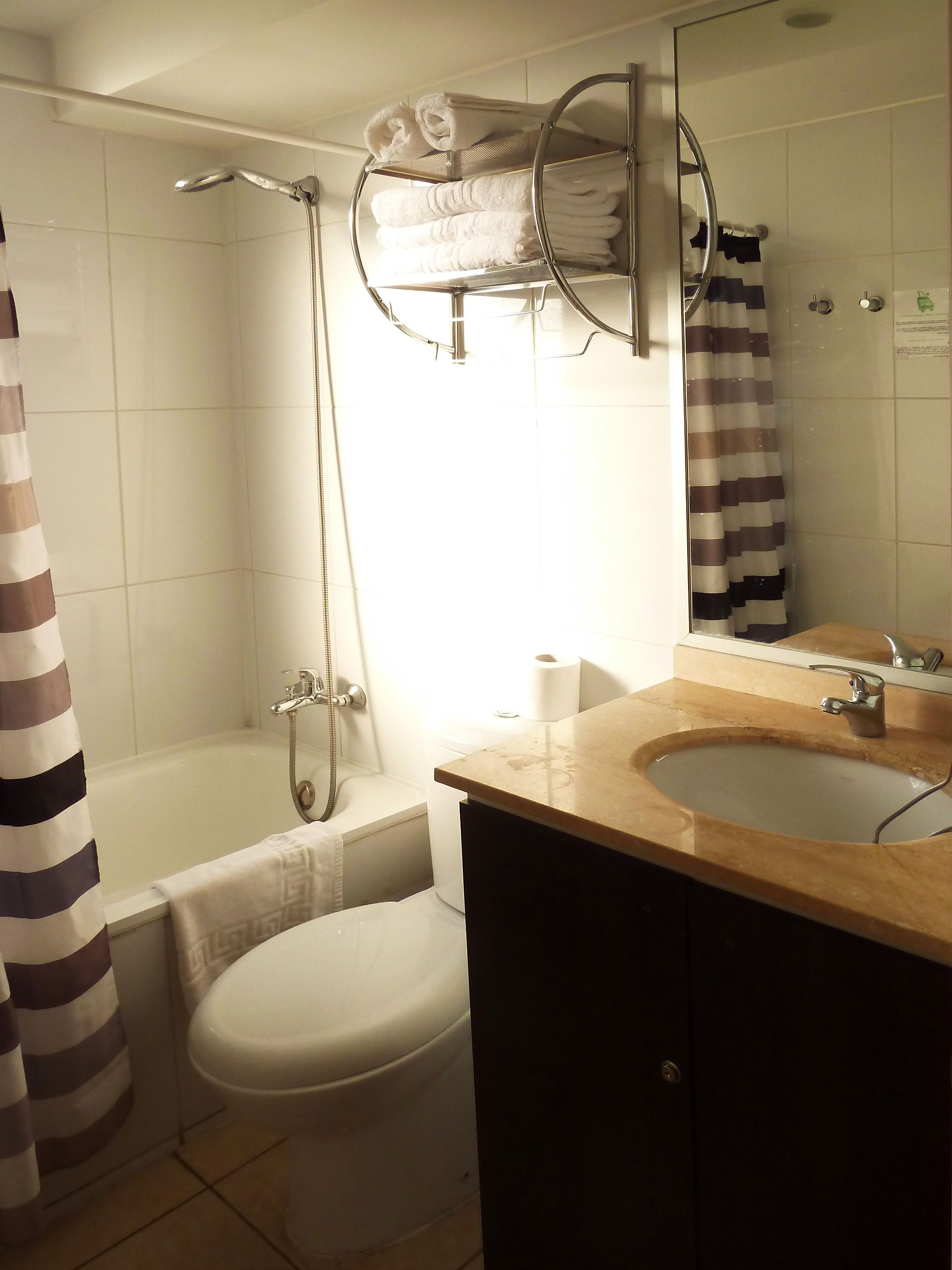 Et badeværelse med badekar, toilet, vask og et håndklædestativ med håndklæder.