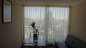 Una sala de estar con una mesa de comedor de vidrio, un sofá de cuero negro y cortinas translúcidas.