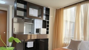Una habitación de hotel compacta con una mesa de comedor de madera, una cama con colcha color crema, un armario empotrado con espejos y una planta en maceta.