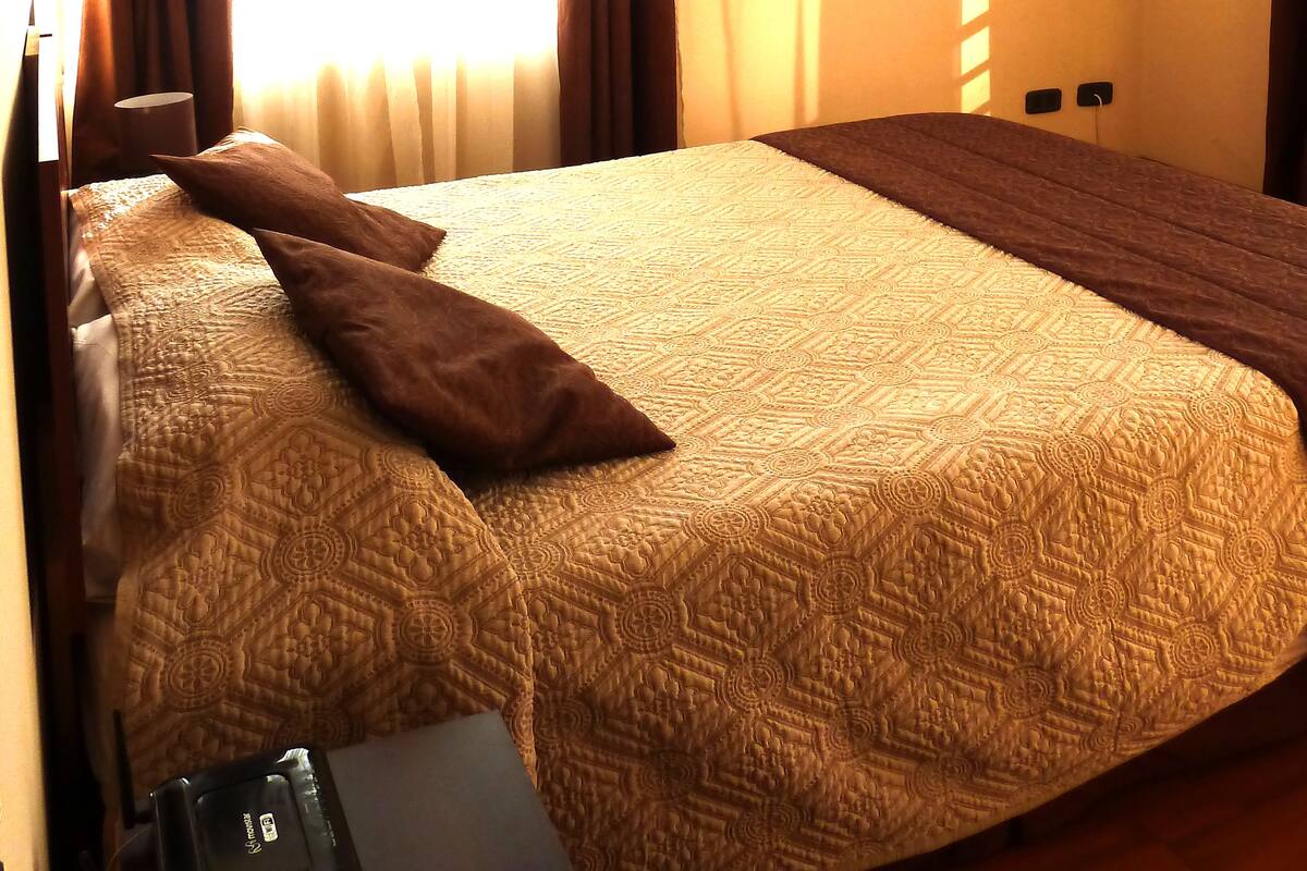 Ein Hotelzimmer mit einem großen Bett, einem Schreibtisch mit Telefon und Maus sowie einem Fenster mit Vorhängen.