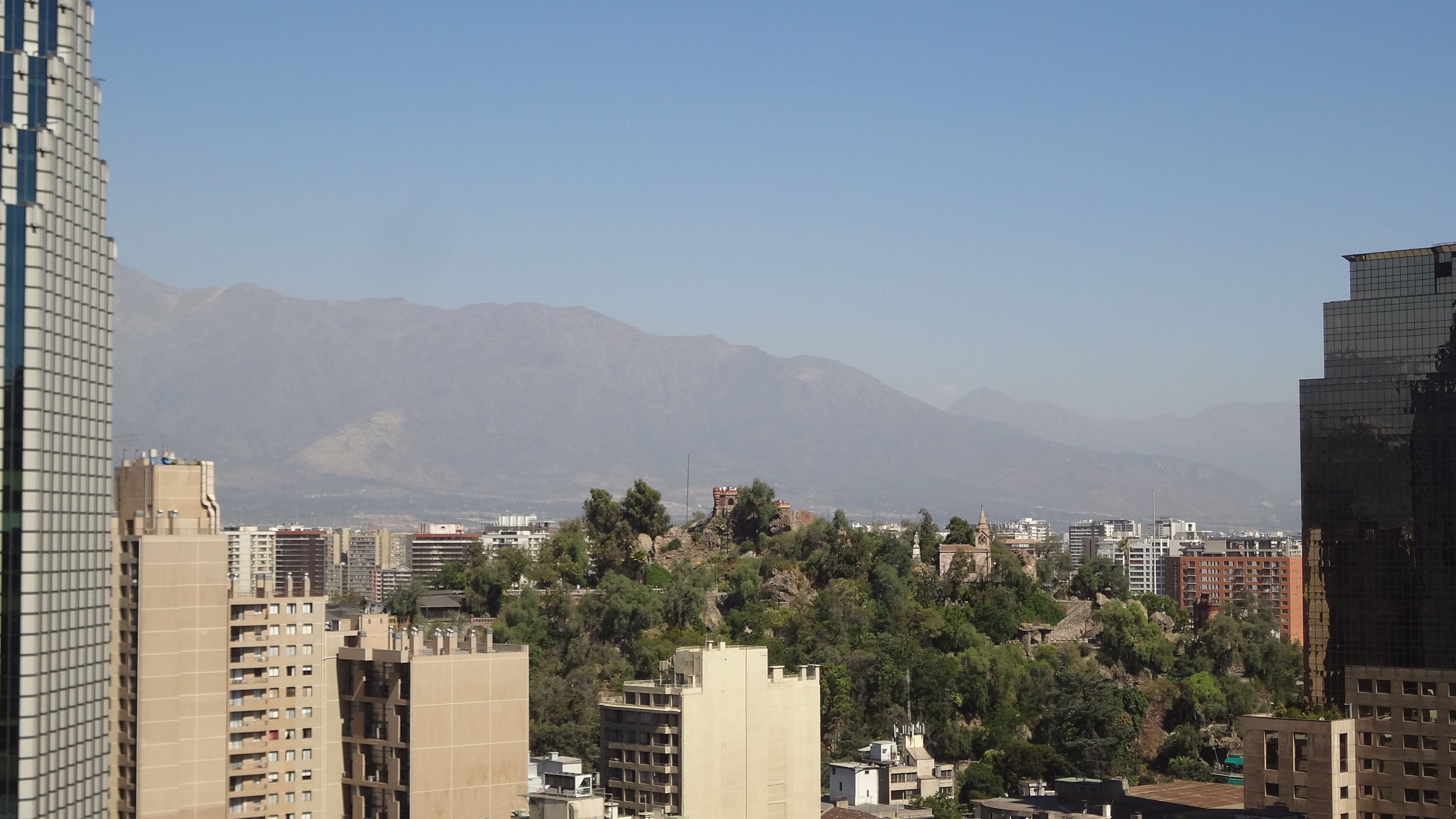 A cityscape with modern high-rise buildings, a mix of residential and commercial structures, and a backdrop of mountains.
