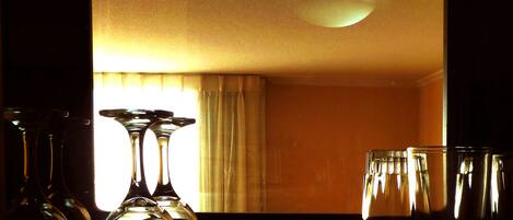 Una habitación con un espejo grande que refleja una ventana con cortinas, una lámpara y varios vasos sobre una mesa.