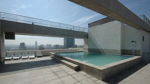 Piscina en la azotea con vistas a la ciudad, mobiliario de hormigón y zona cubierta.