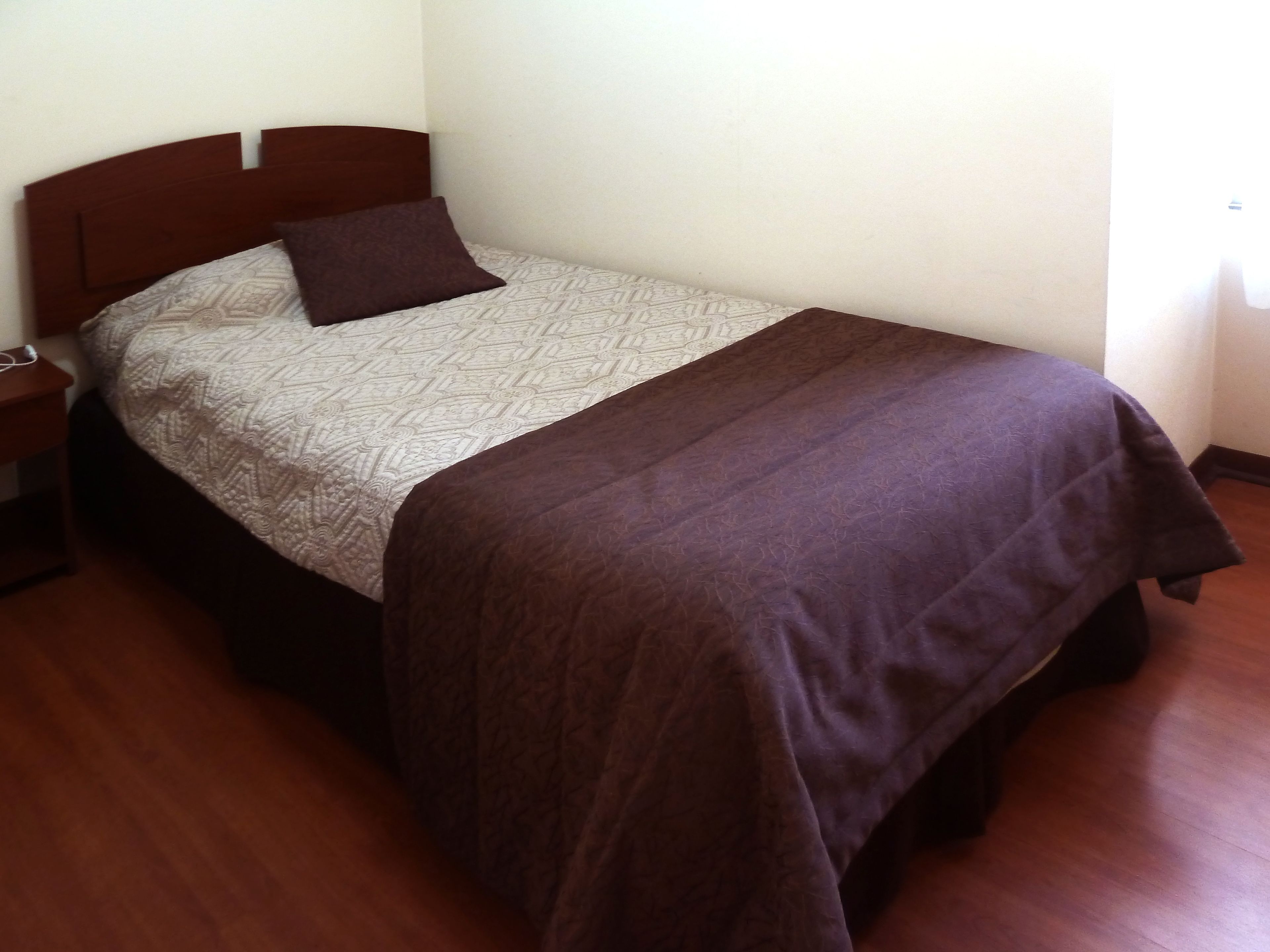 A single bed with a patterned bedspread, a brown pillow, and a brown blanket.