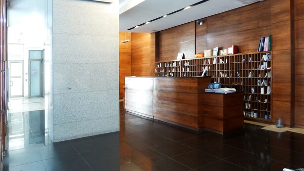 Un área de recepción moderna con un mostrador de madera, una barra blanca y una estantería fijada a la pared.
