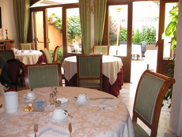 Un comedor con mesas redondas, sillas y vistas al jardín a través de amplios ventanales.