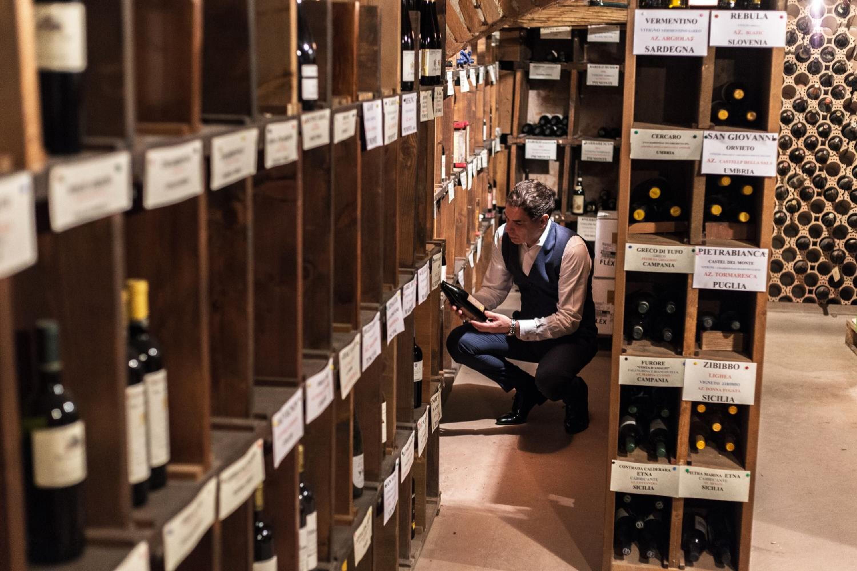 A wine cellar with wooden shelves and labels indicating different wine varieties.