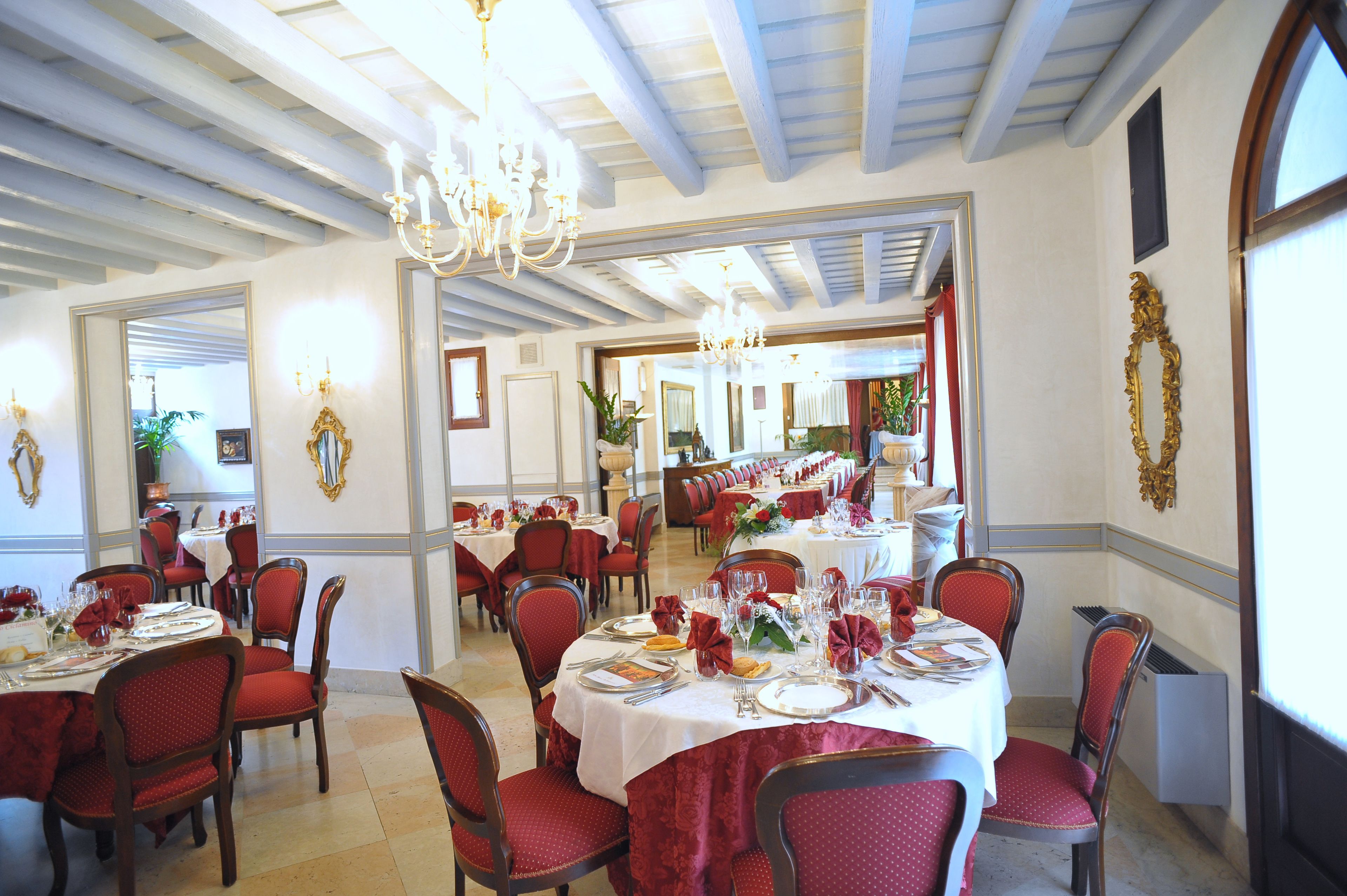 Zona pranzo con tavoli rotondi, sedie imbottite rosse e lampadari.