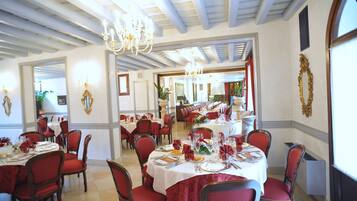 Zona pranzo con tavoli rotondi, sedie imbottite rosse e lampadari.