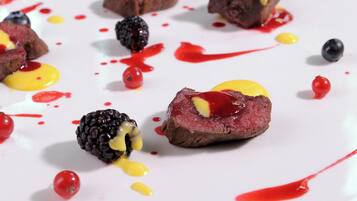 Een dessertborden met vleesschijf, gegarneerd met bramen en gele saus, omringd door bessen en rode saus.