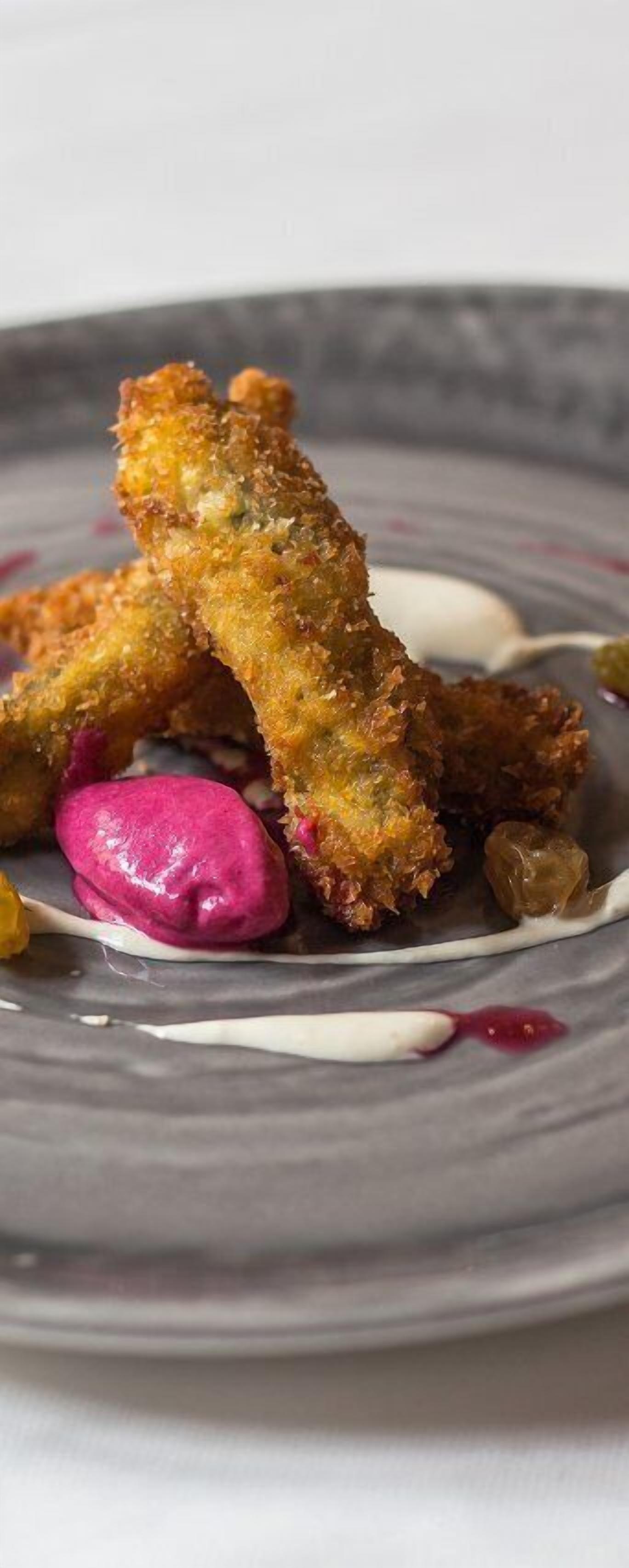 Een bord met paneer en gebakken gerechtjes, mogelijk chicken tenders, met een toef roze saus en wat augurken.