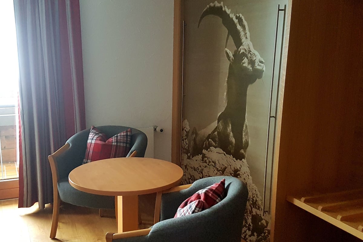 A room with a round wooden table, two armchairs, a plaid pillow, and a large wall mural of a llama.