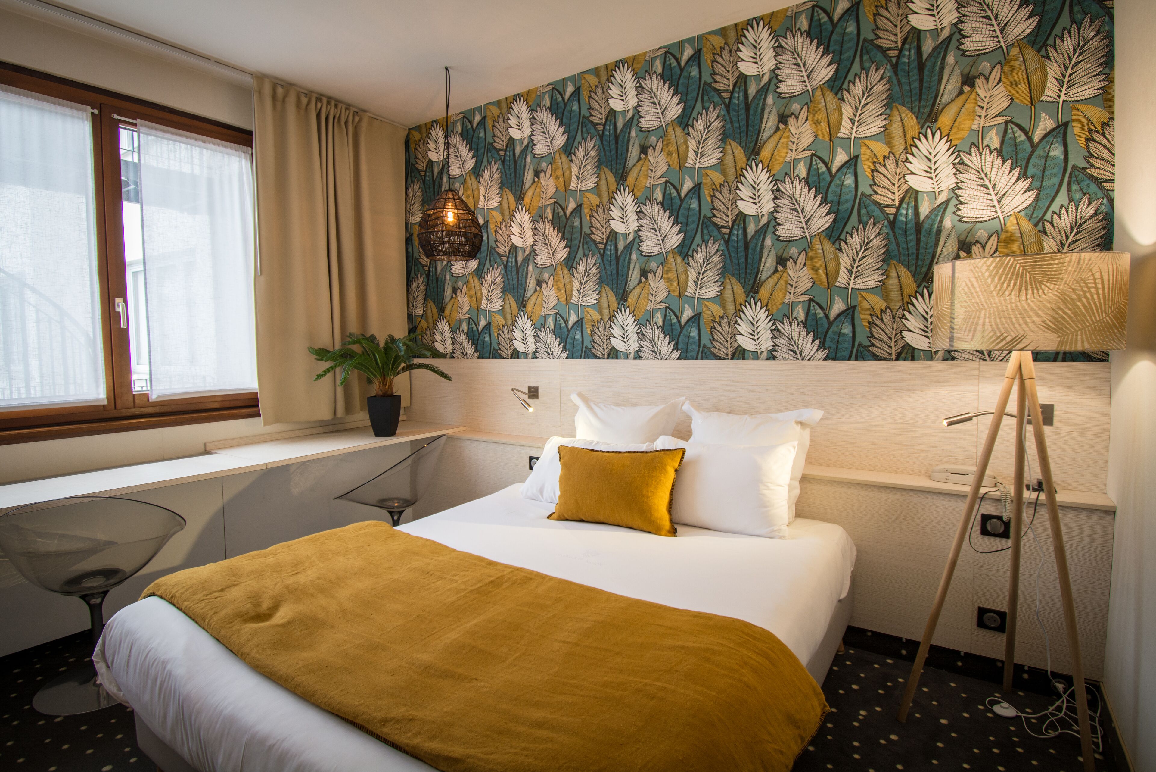 Habitación de hotel con cama, escritorio, planta en maceta y pared con diseño.