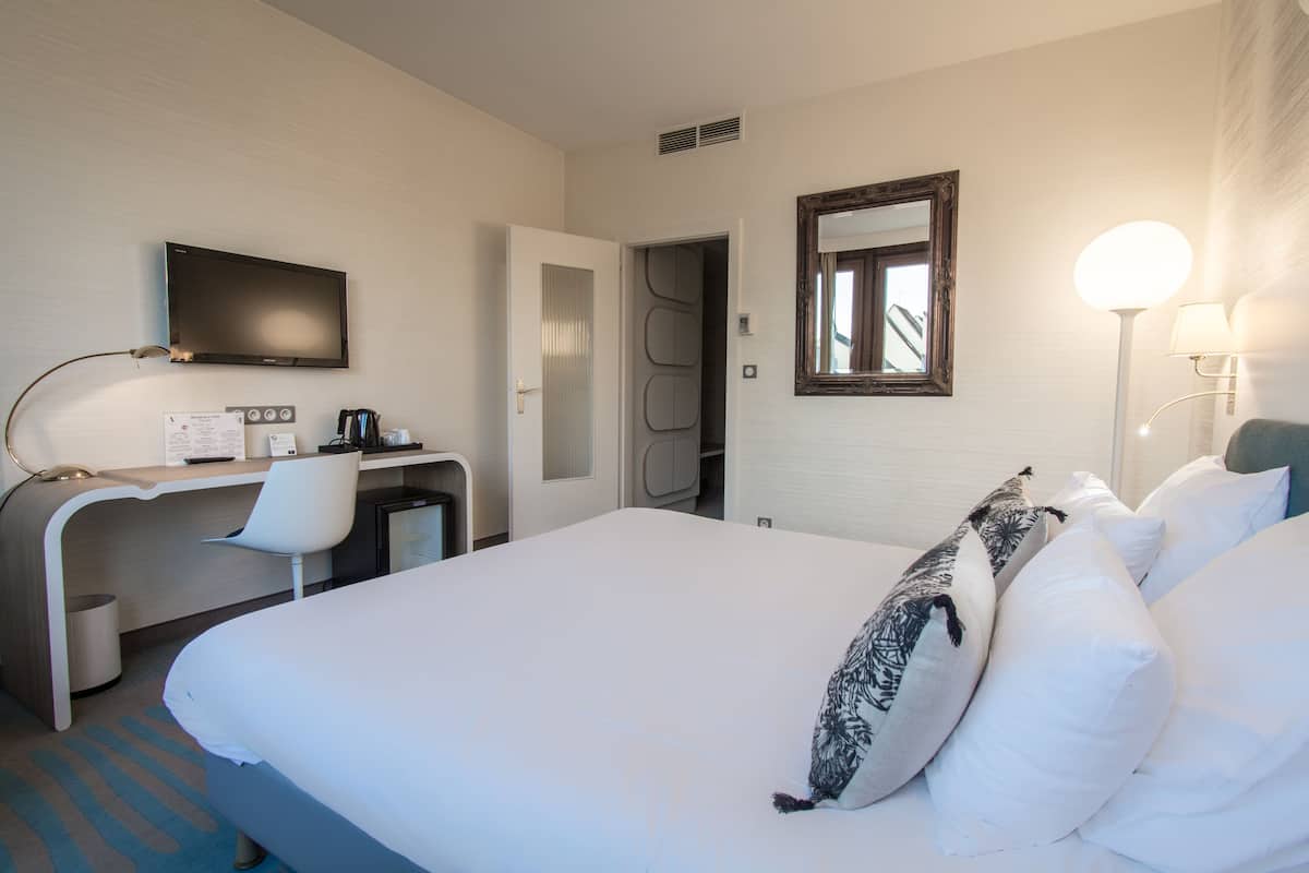 Een hotelkamer met een bed, een bureau met stoel, een televisie, een spiegel en een lamp.