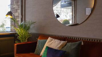 A modern living room with a brown leather sofa, a round mirror, and a potted plant.