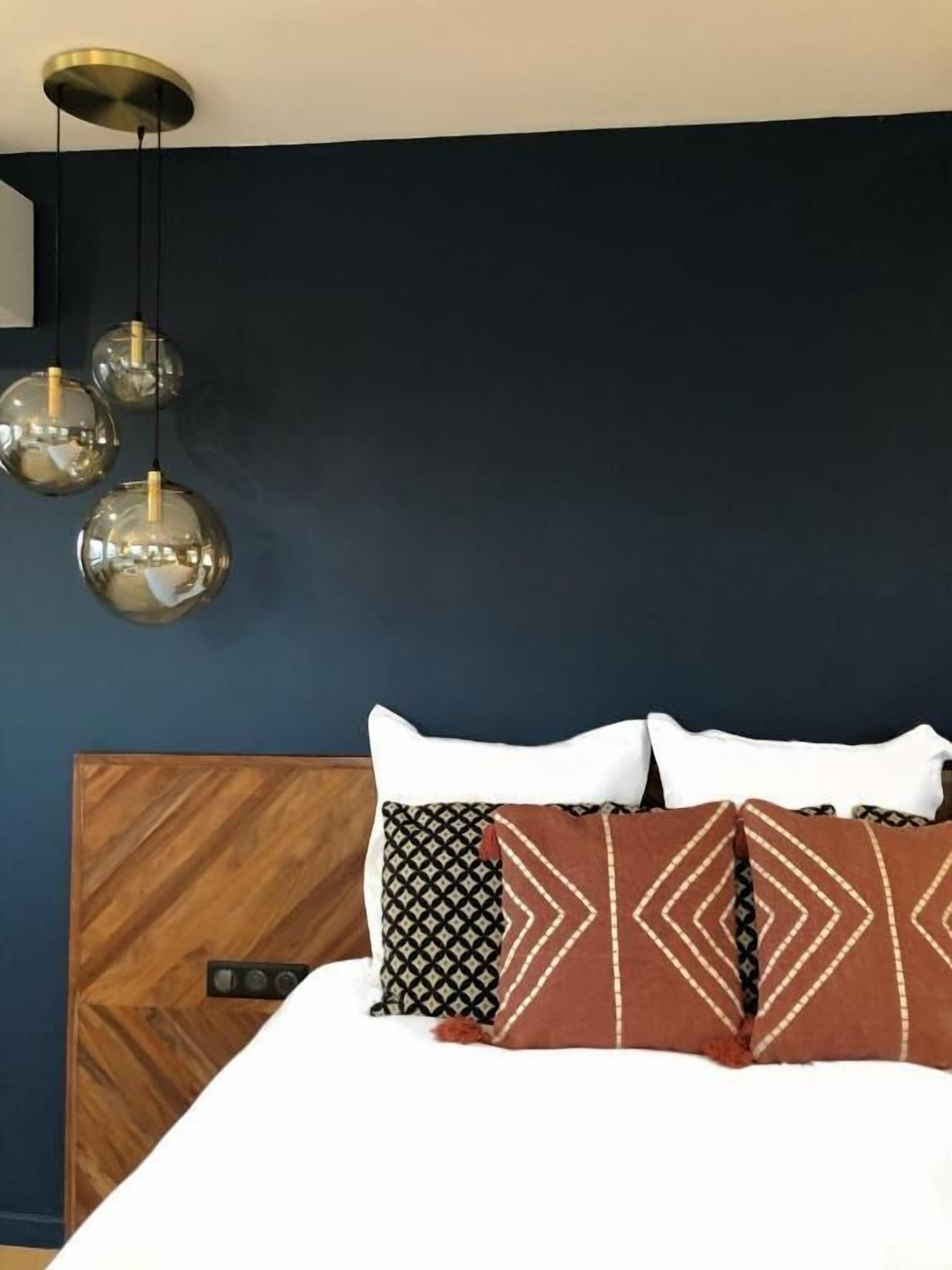 A bedroom with a dark blue wall, a wooden headboard, and three spherical pendant lights.