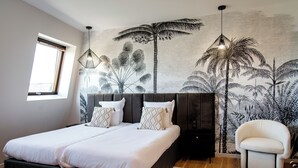 Un dormitorio con dos camas, un ventanal grande, un mural de palmeras y una silla moderna.