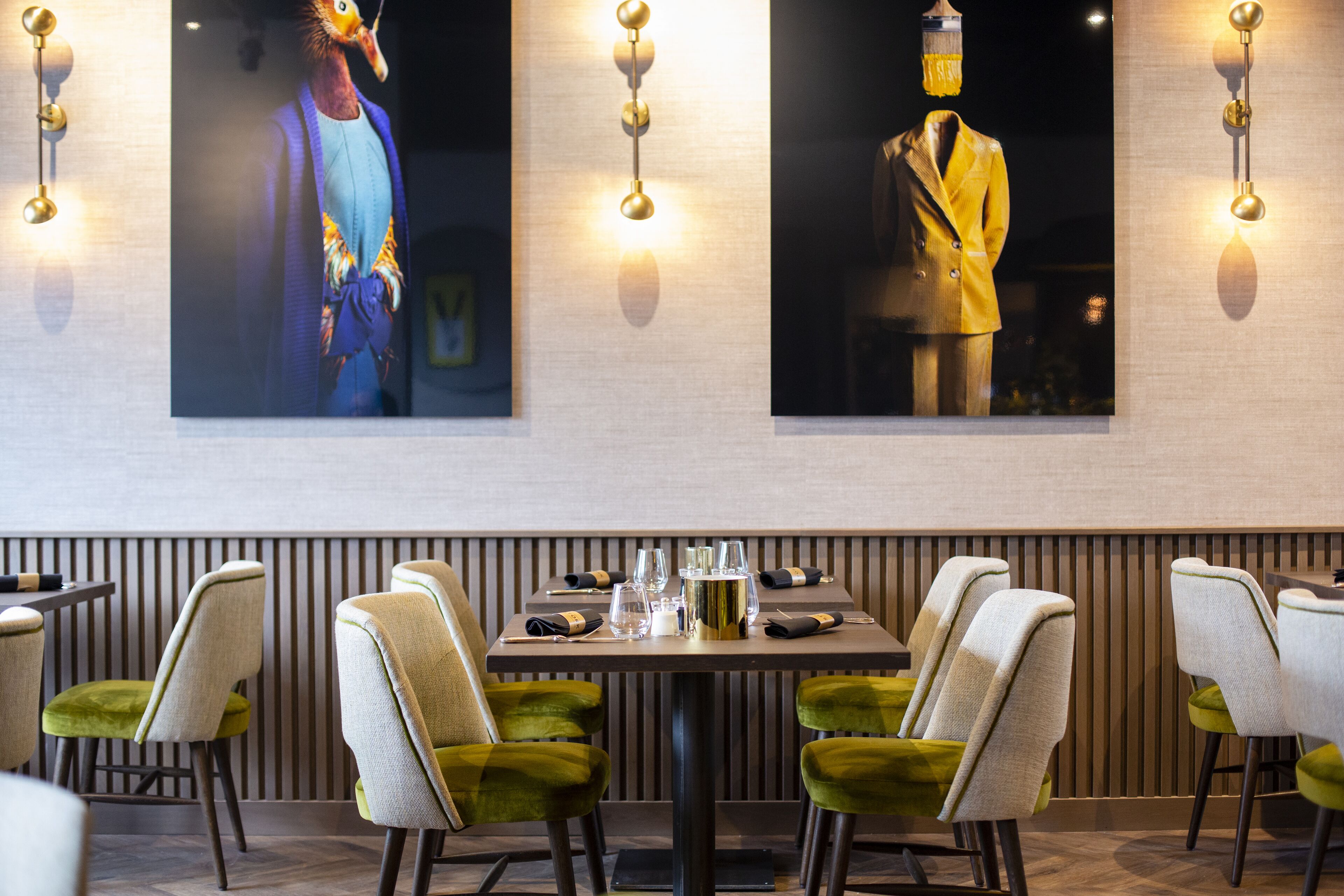 Un restaurant avec une longue table dressée pour le repas, entourée de chaises à l’assise rembourrée de tissu vert.