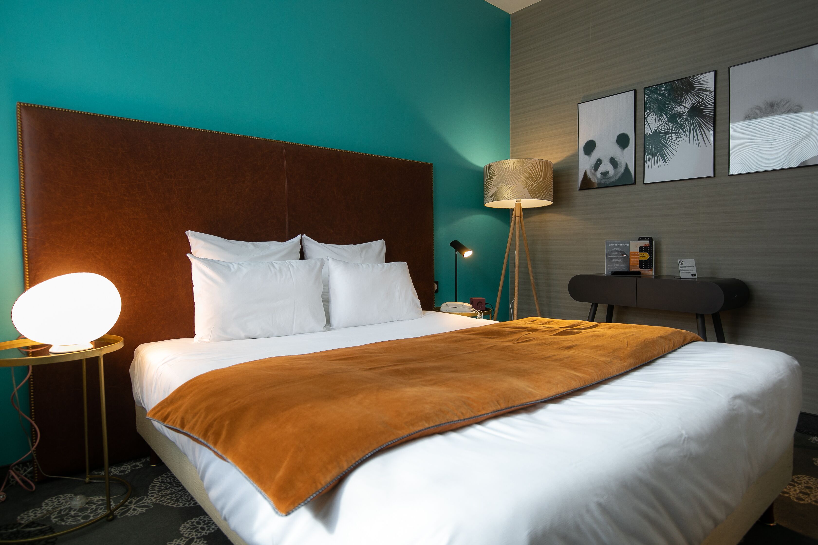 A neatly made bed with white linens and a brown throw blanket, a bedside lamp, and a wall-mounted lamp.