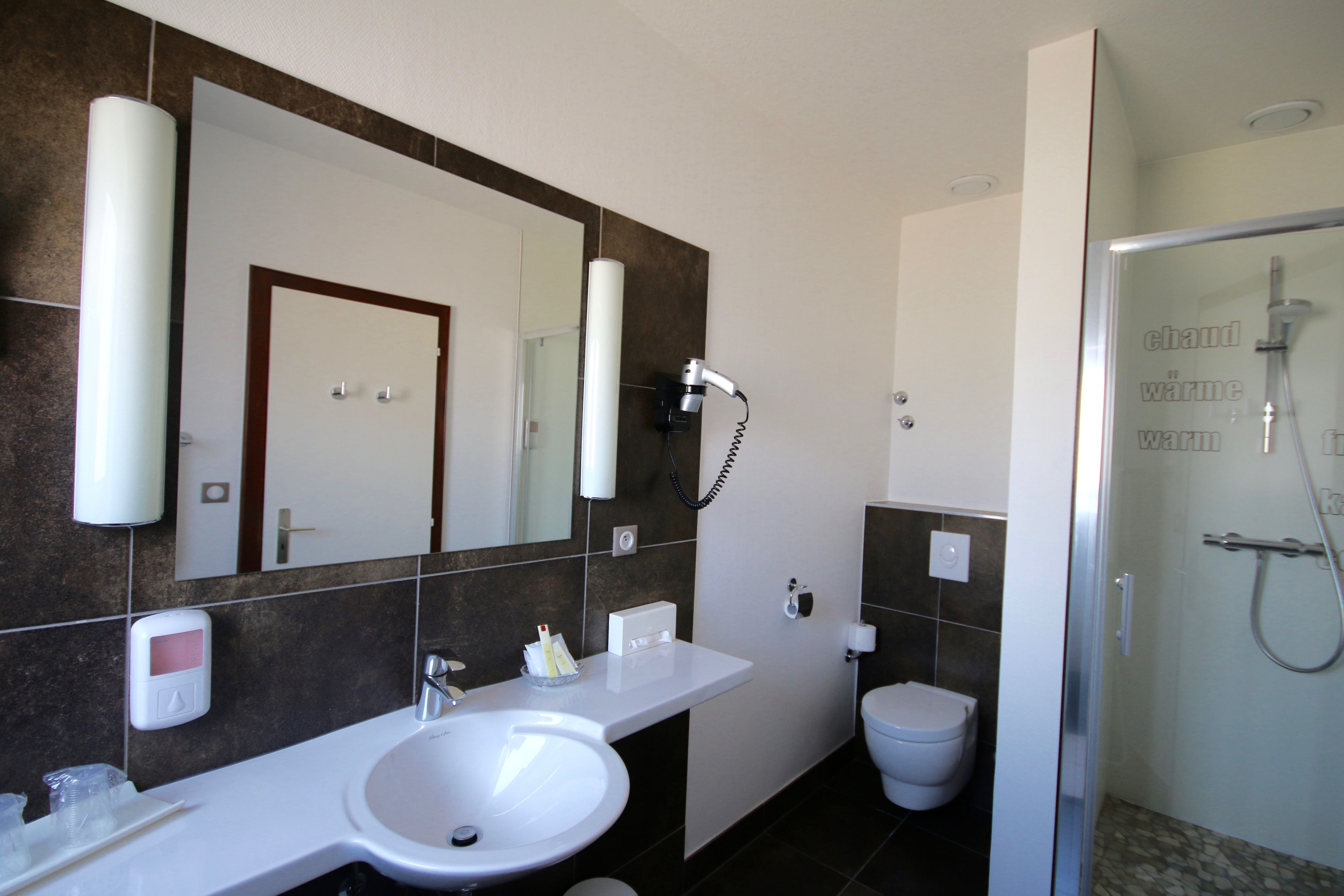 A modern bathroom with a large mirror, a sink, a toilet, and a shower area.