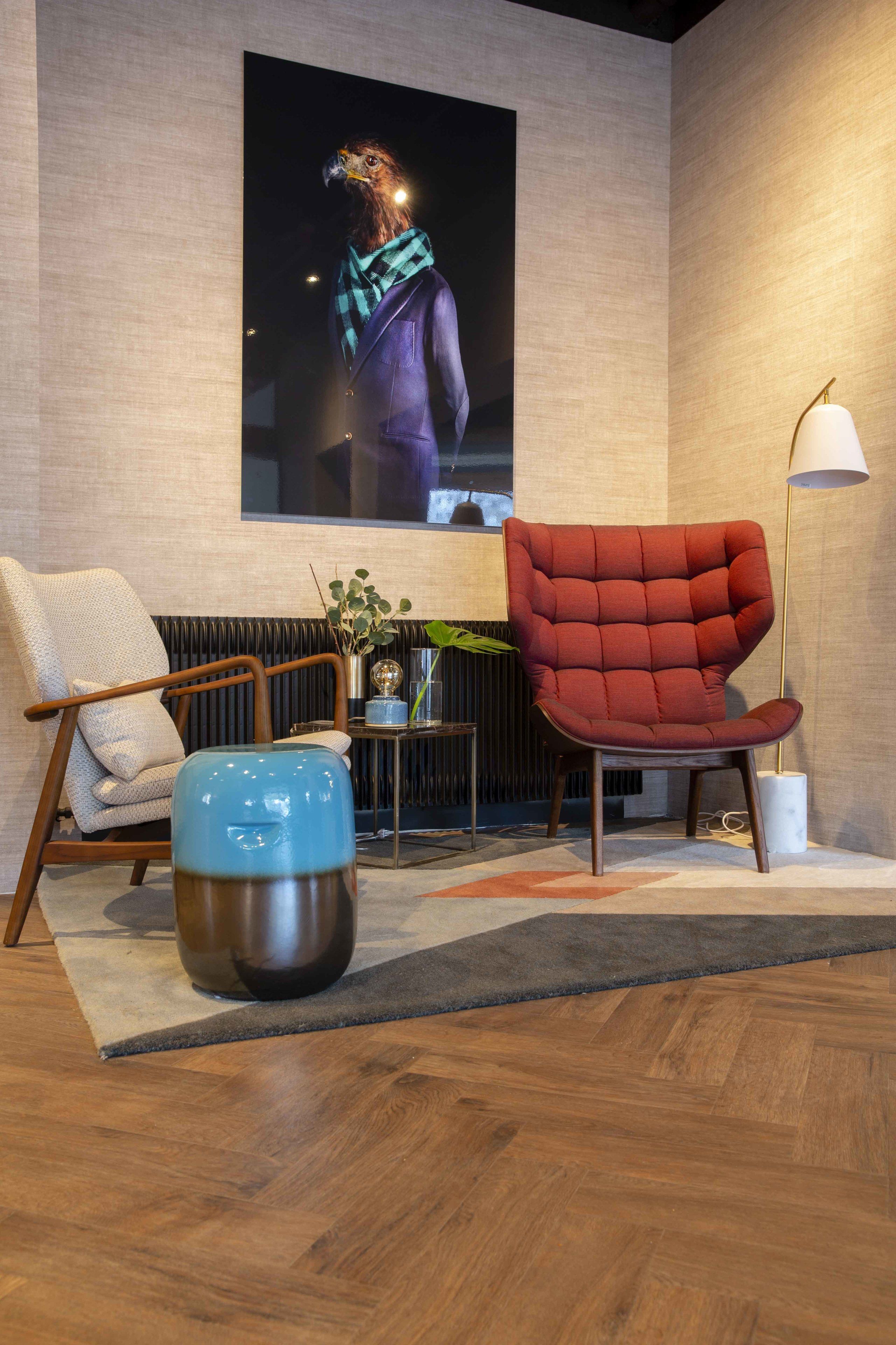 Un salón moderno con un sillón rojo, un reposapiés azul y un cuadro abstracto grande en la pared.