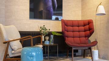 Un salón moderno con un sillón rojo, un reposapiés azul y un cuadro abstracto grande en la pared.