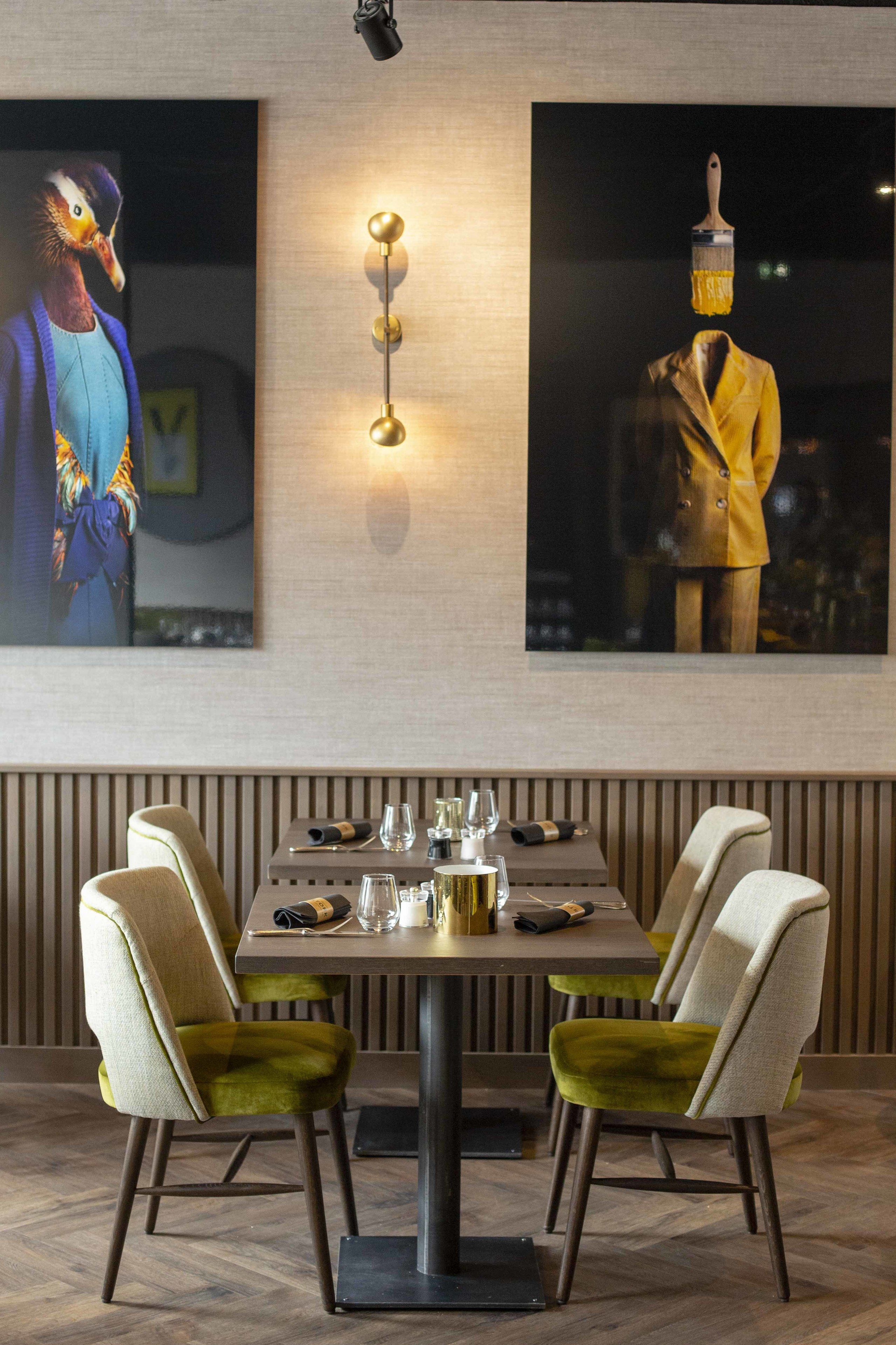A dining area with a table set for two, chairs with green upholstery, and a wall-mounted light fixture.
