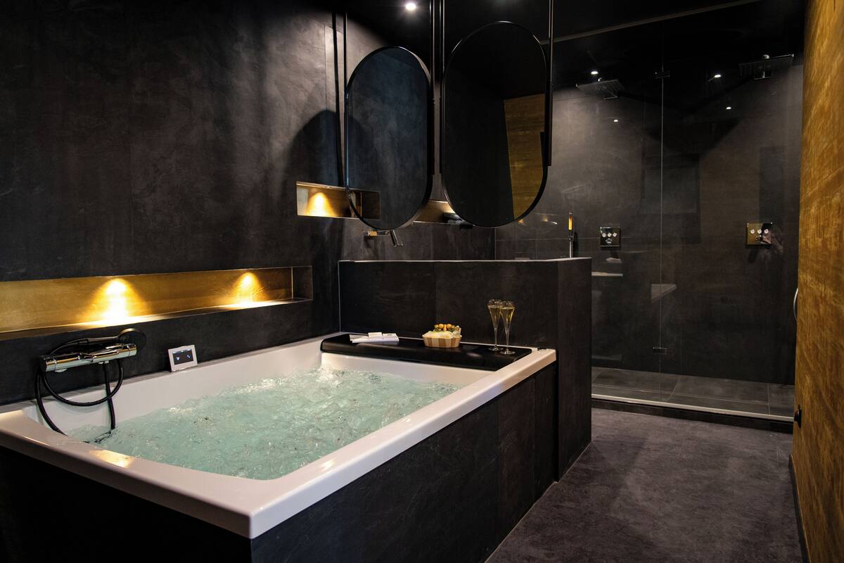 Een moderne badkamer met een groot bad, twee spiegels aan de muur en een douchecabine met glazen wanden.