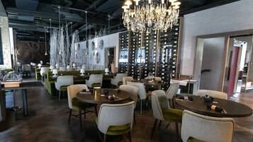 Uma área de jantar moderna com mesas redondas, cadeiras verdes e brancas, e um candelabro.