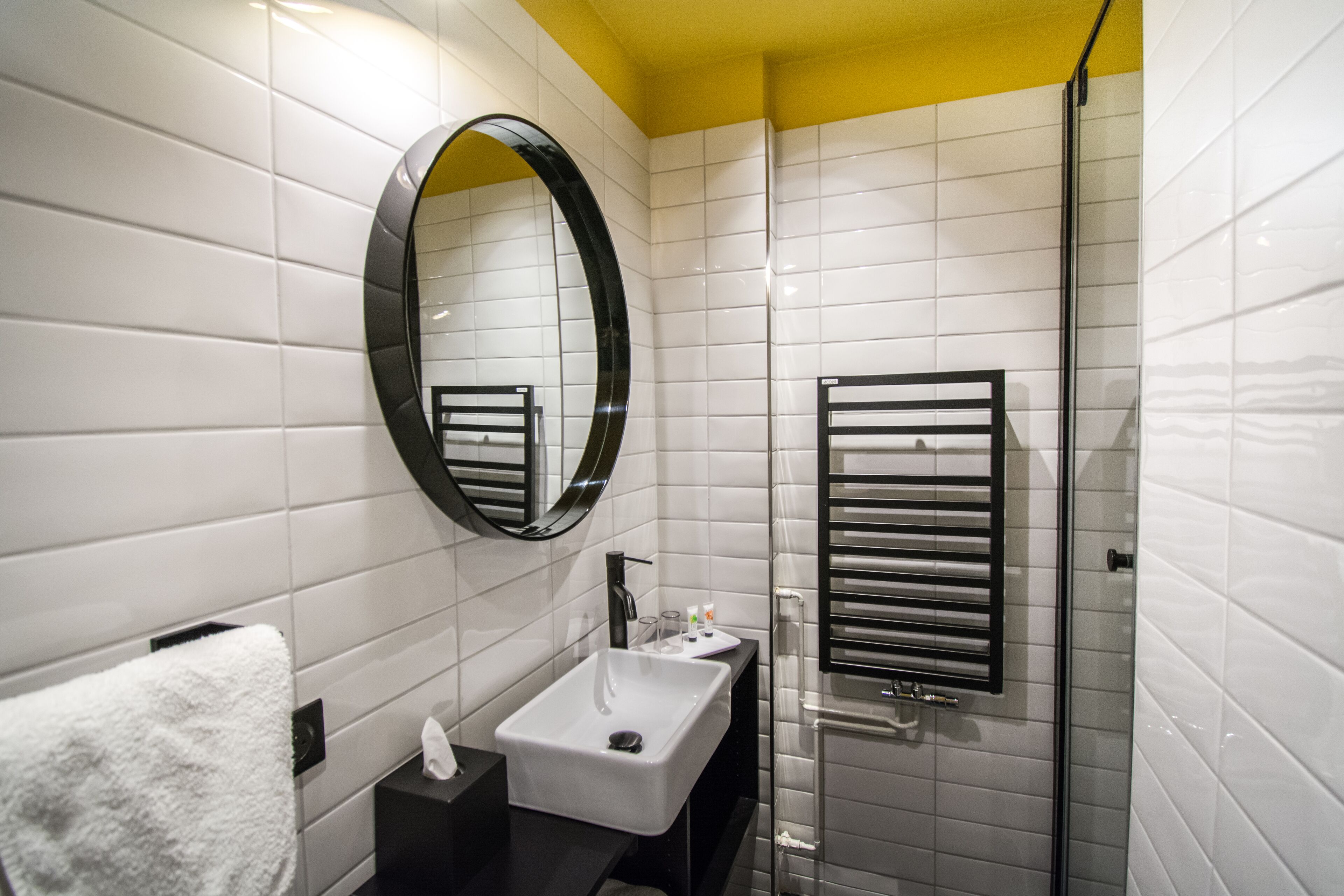 A modern bathroom with white tiled walls, a black-framed mirror, a white sink, and a glass-enclosed shower.